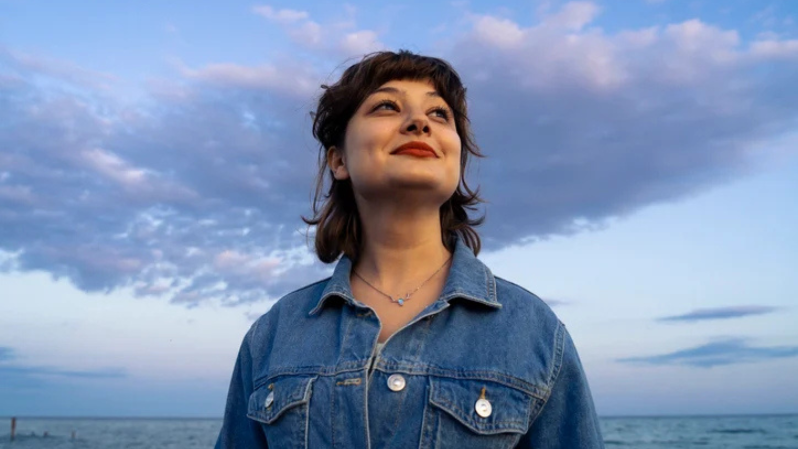 Illustrative image of a smiling person holding their head up high against a cloudy background.
