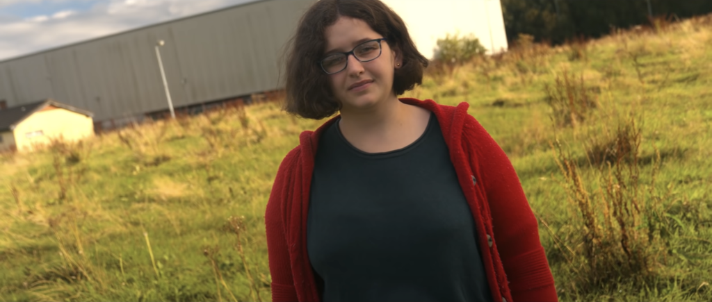 Video thumbnail of a person looking directly into the camera in a grassy field.