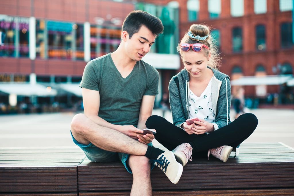 Illustrative image of two people sitting together in an urban setting, smiling and viewing their phones.