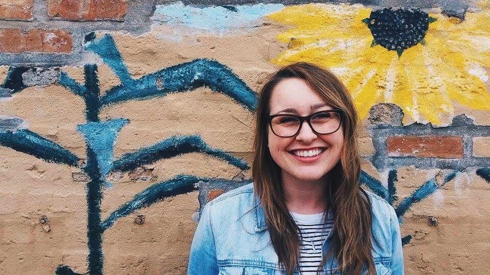 Illustrative image of a smiling person standing against a painted outdoor wall.