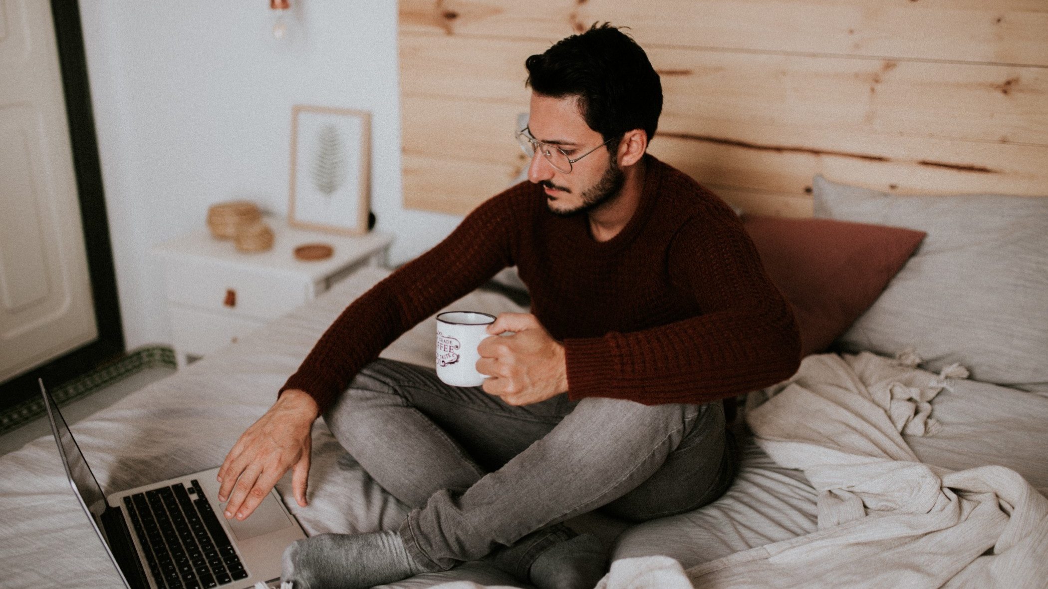 Illustrative image of a person lounging in bed with a laptop and  hot drink.