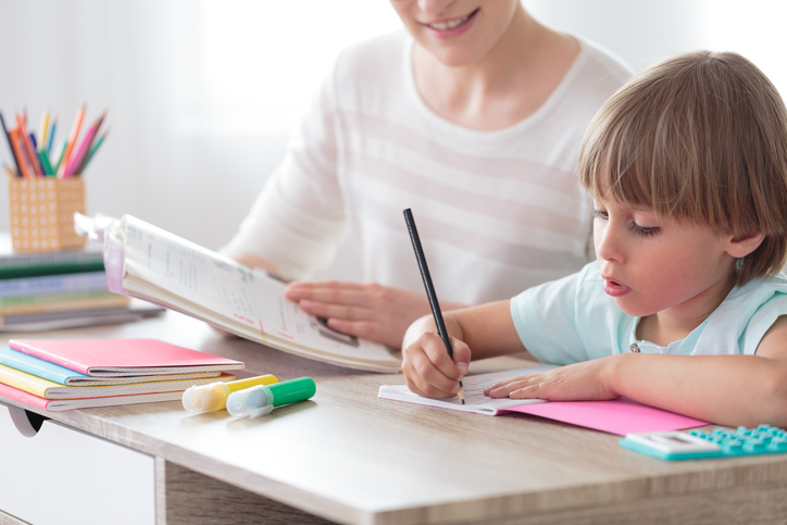 Illustrative image of a child focusing on homework with an adult in the background.
