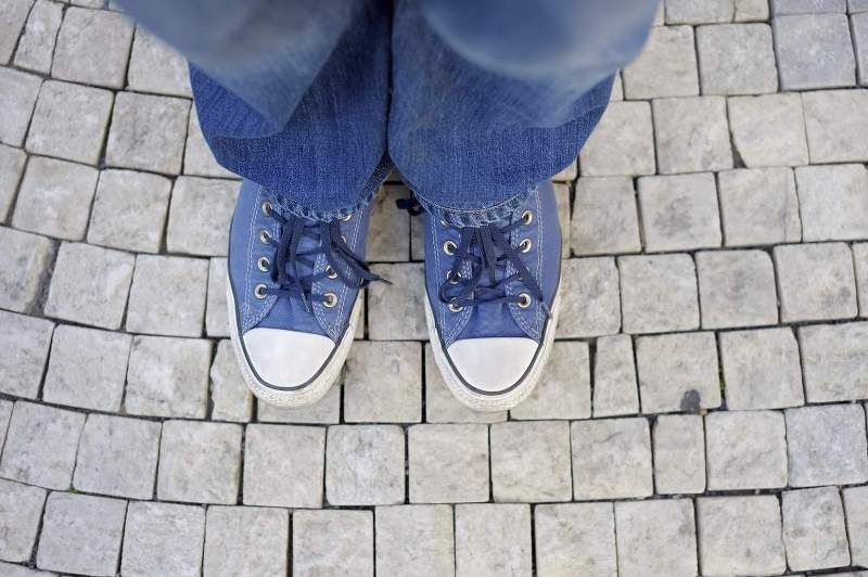 Illustrative image showing only a person's shoes as they stand on a pavement.