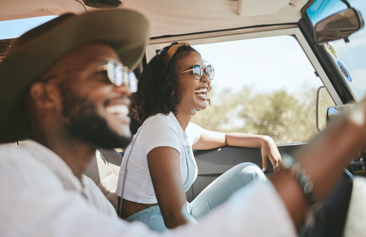 Illustrative image of a smiling couple in a car driving through the countryside.