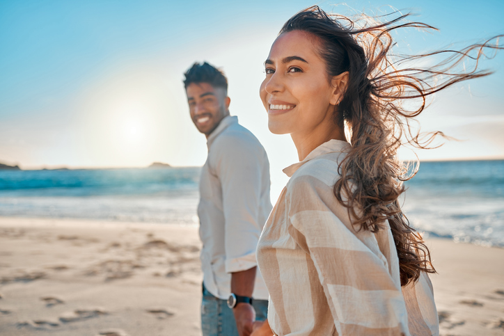 Illustrative image of a smiling person walking on a beach with another person in the background.