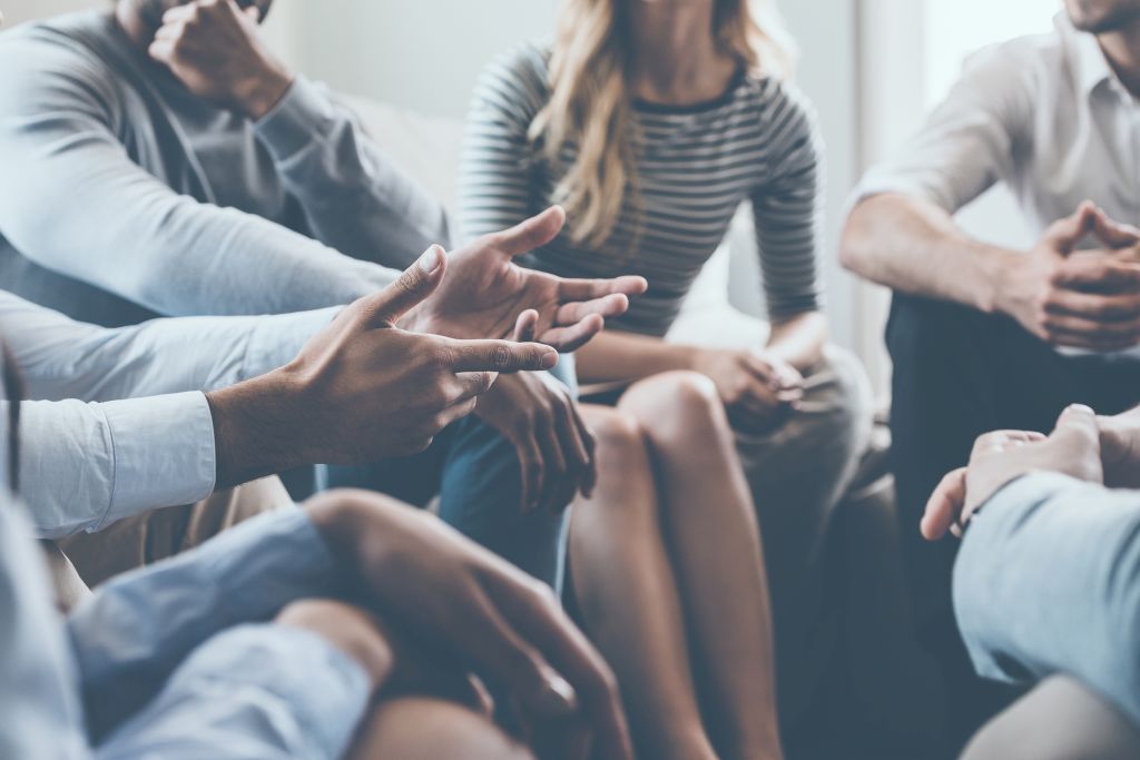 Illustrative image of a group of people, with a close-up focus on their hands gesturing as they speak.