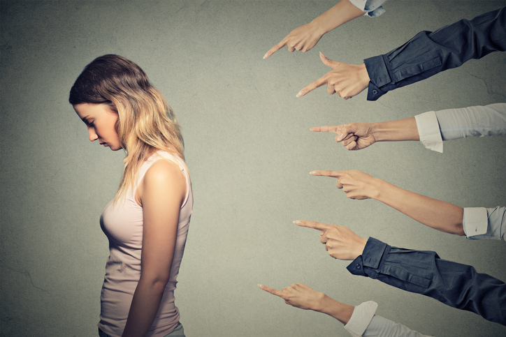 Illustrative image of 6 different hands pointing towards a sad person with back turned and head bowed.