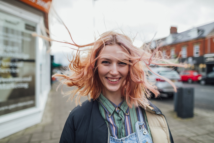 Illustrative image of a person smiling outside with their hair blowing in the wind.