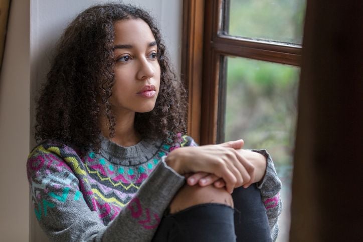 Illustrative photo of a person sitting in a window, looking out