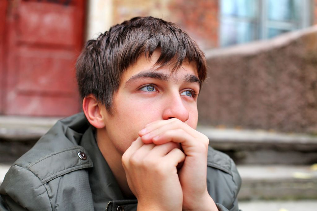 Illustrative image of a person sitting on outdoor steps, hands clasped at their mouth, staring into the distance.