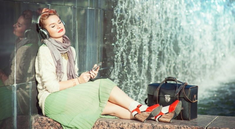 Illustrative photo of a person sitting by a fountain with their eyes closed, listening to their headphones.