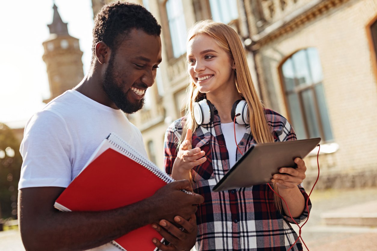 Illustrative image of two people, one carrying a notebook and the other carrying a tablet, smiling and chatting.