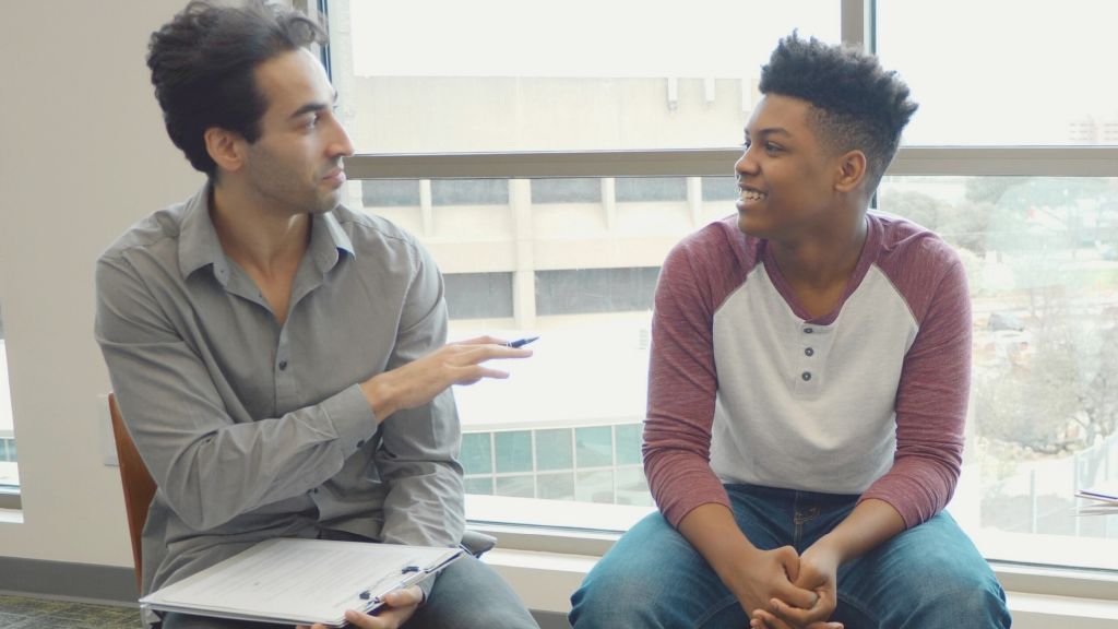 Illustrative image of two seated people conversing, one holding a clipboard.