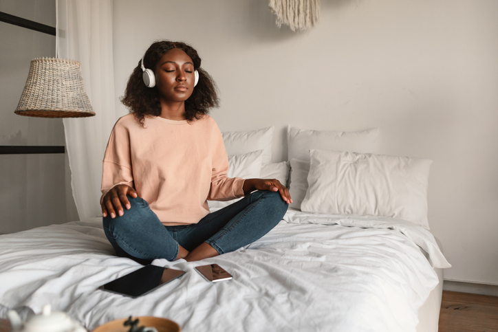 Illustrative image of a calm person with headphones sitting cross-legged on a bed.