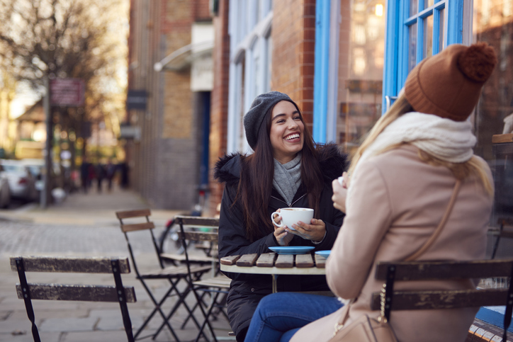 Illustrative image of two friends sitting and chatting outside a coffee shop.