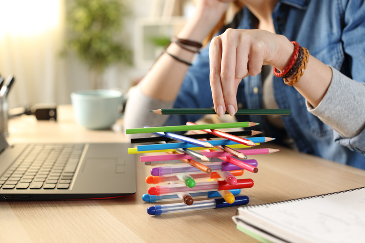 Illustrative image of a person building a pencil tower while seated in front of their laptop.