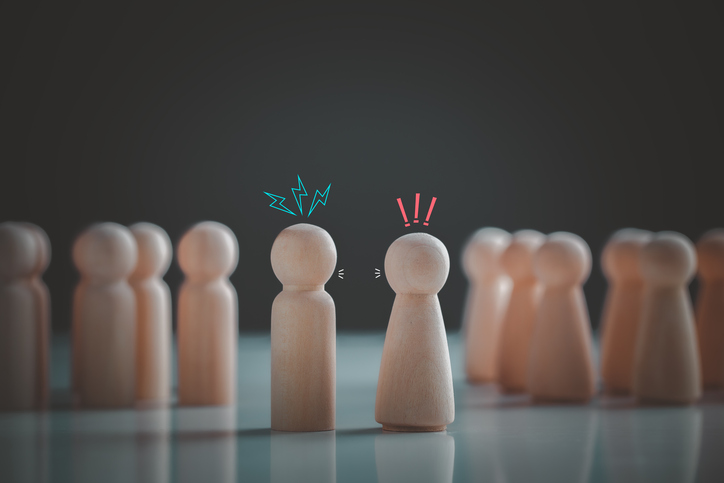 Illustrative image of two wooden figures in conflict against a dark background of other wooden figures.