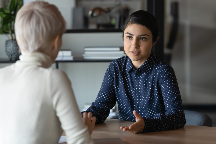 Illustrative image of two people sitting across from each other and conversing in an office.