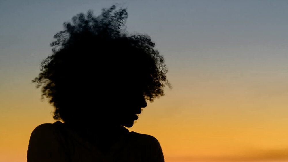 Illustrative image of a silhouetted person with head turned to the side against a sunset-like background.