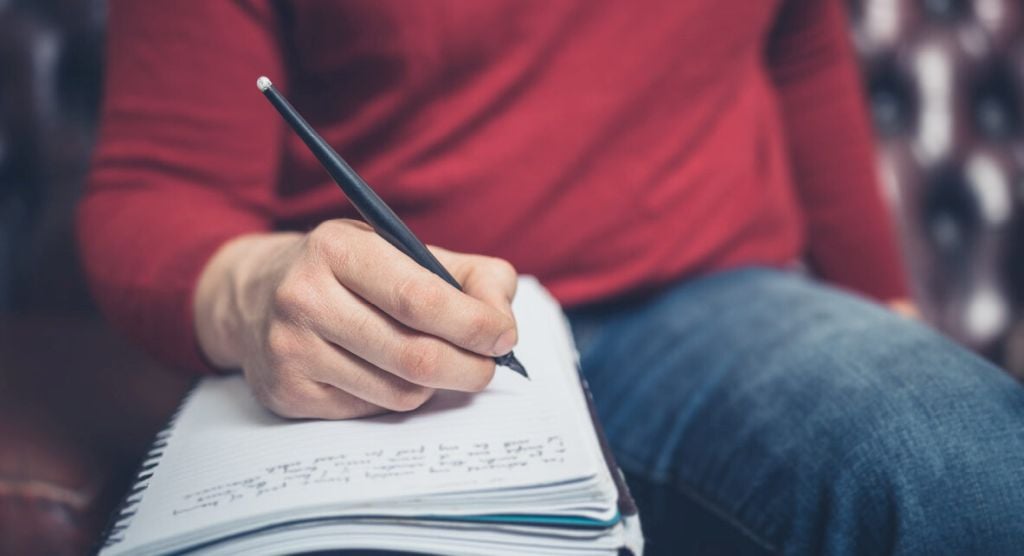 Illustrative image of a person's hand writing in a journal.