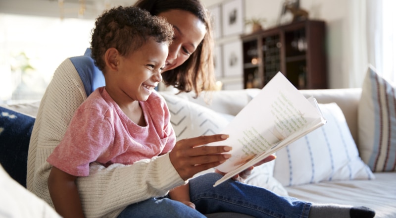 Illustrative image of a person reading to a child sitting on their lap.