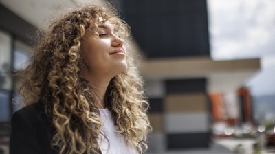 Illustrative image of a person inhaling deeply and smiling with eyes closed outside.