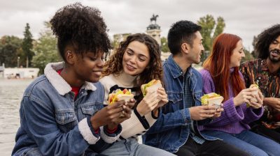 Illustrative image of a group of people eating sandwiches together outside.