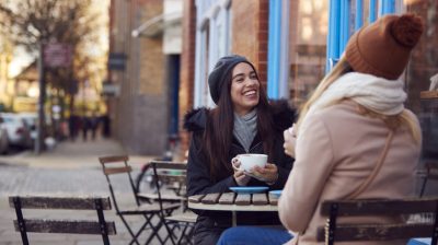 Illustrative image of two friends sitting and chatting outside a coffee shop.