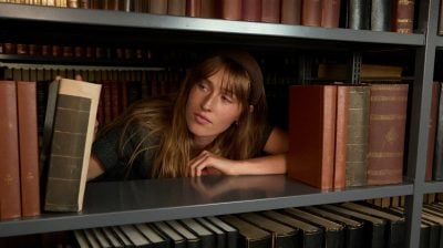a person peers between books on a bookshelf