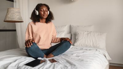 Illustrative image of a calm person with headphones sitting cross-legged on a bed.