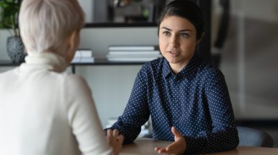 Illustrative image of two people sitting across from each other and conversing in an office.