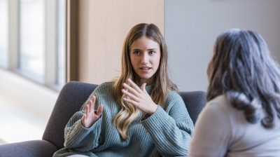 Illustrative image of two seated people talking together indoors.