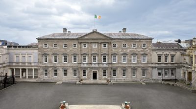 A view of Leinster House, the seat of parliament for TDs in Ireland, a grey building against a blue-grey sky.