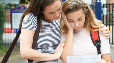 Illustrative image of a sad person reading from a sheet of paper, while being consoled by another person.