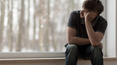 Illustrative image of a sad person sitting and looking out a window.