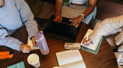 Students around a table of books, notebooks, water and warm beverages