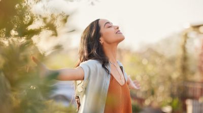 Illustrative image of a person standing mindfully in nature with arms outstretched, eyes closed, and head tilted back slightly.