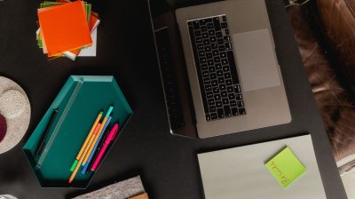 A desk with a laptop, pens, post it notes and other study materials