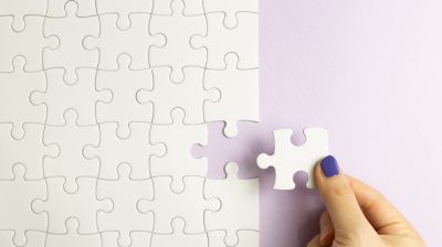 Illustrative image of a set of white puzzle pieces with a hand holding last one piece on purple background.