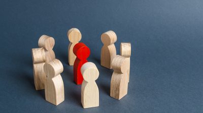 Red wooden figure surrounded by a circle of light brown wooden figures.
