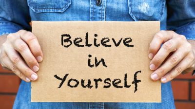 Illustrative image of a person holding up a cardboard sign that says: "Believe in yourself."