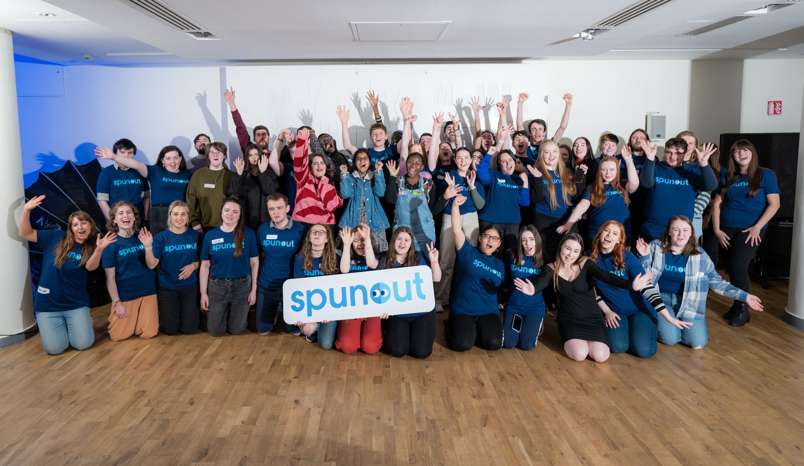 Group picture of spunout volunteers with a spunout card lifted by the volunteers at the front of the image