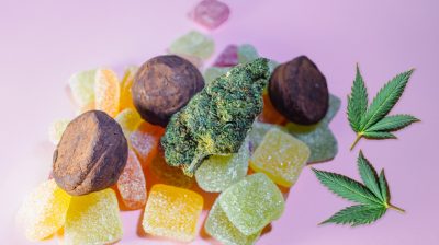 cannabis leaves and Candies Infused with CBD HHC or THC on a baby pink background.