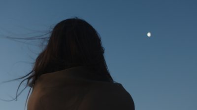 silhouette of a feminine figure with long hair looking up at the moon