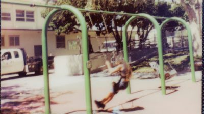 a grainy film photo of a person on a green metal swingset
