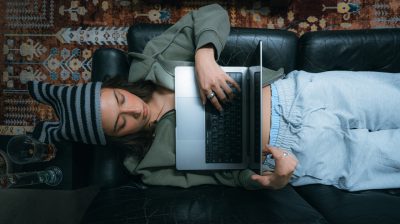 birds eye view of young person lying on couch browsing on their laptop