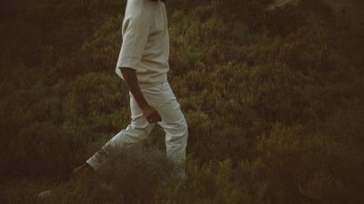 a person walking through long grass wearing a white tshirt and jeans