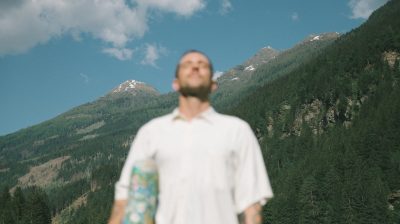 A man standing outdoors with a scenic mountain landscape in the background