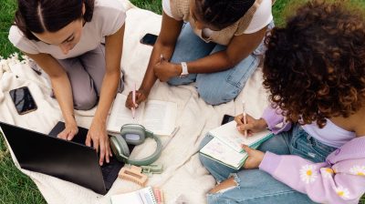 Three friends studying outside using a laptop and notepads
