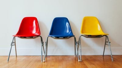a row of brightly coloured chairs, red, blue, yellow, lined up against a white wall.